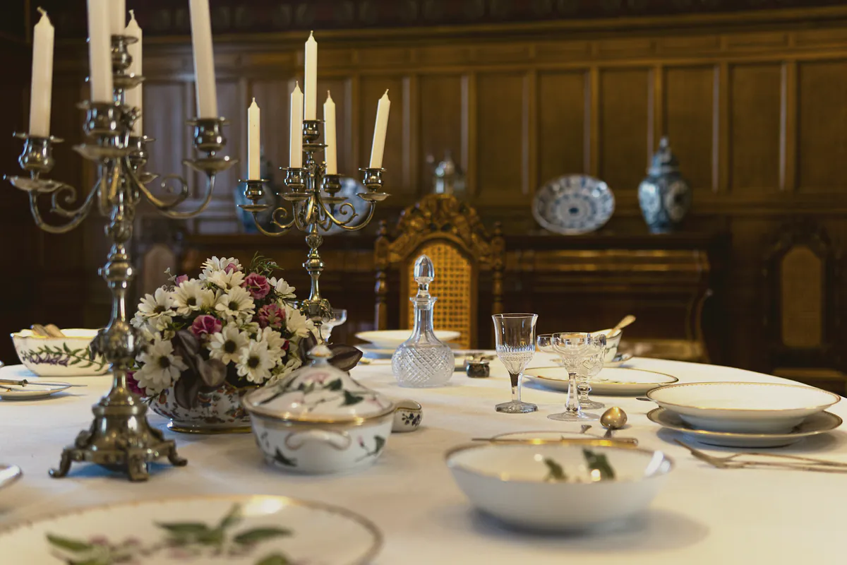 A long dining table laid with fine china, crystal and silver candelabras around a bowl of daisies and roses