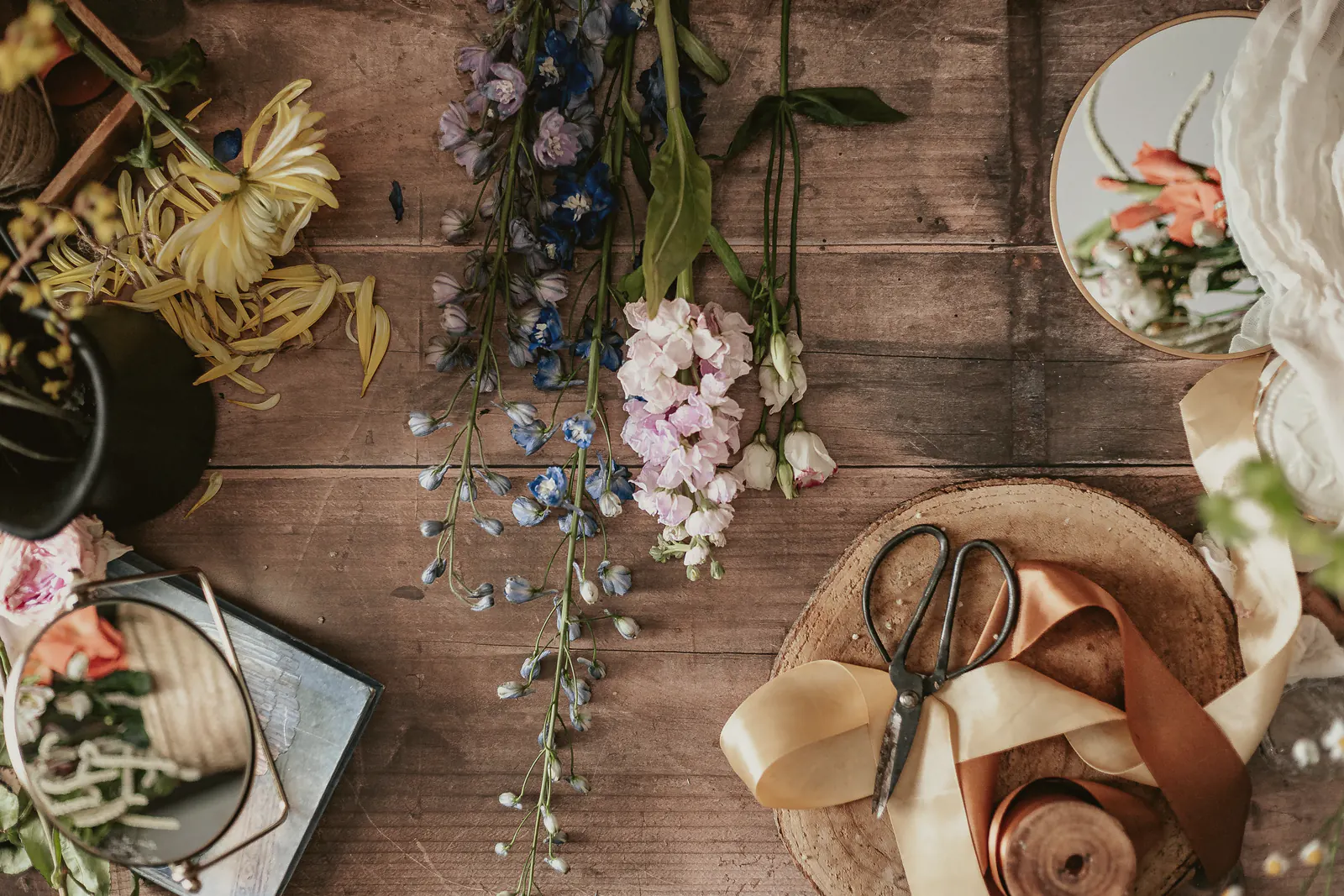 A florist’s timber bench scattered with delphinium, stock, garden roses, ribbon and scissors
