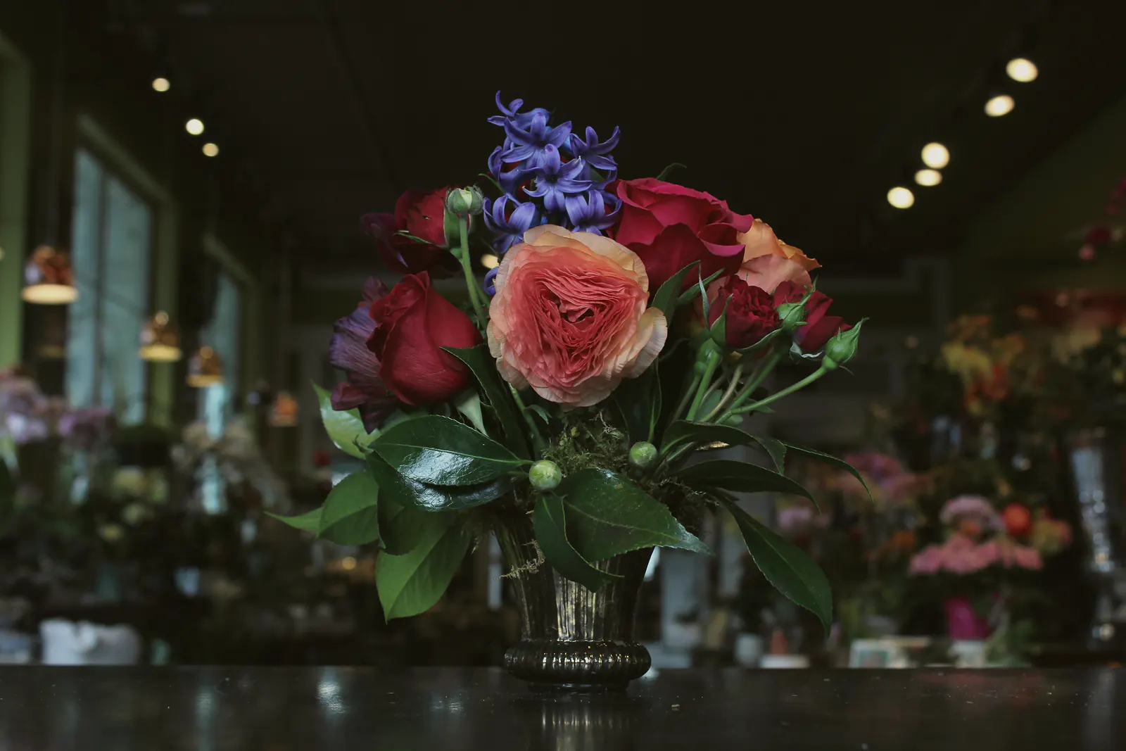 A glowing bouquet of garden roses, ranunculus and hyacinth on the counter of a florist at night