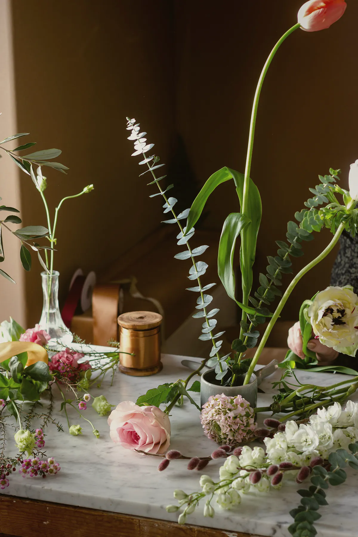 Single stems of tulip, rose and eucalyptus in small glass bottles on a marble shelf