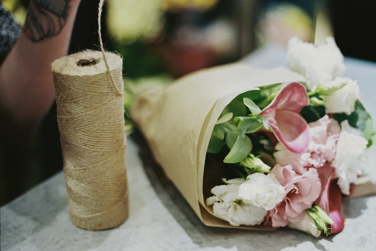 A paper wrapped bouquet of pink and white flowers beside a spool of twine