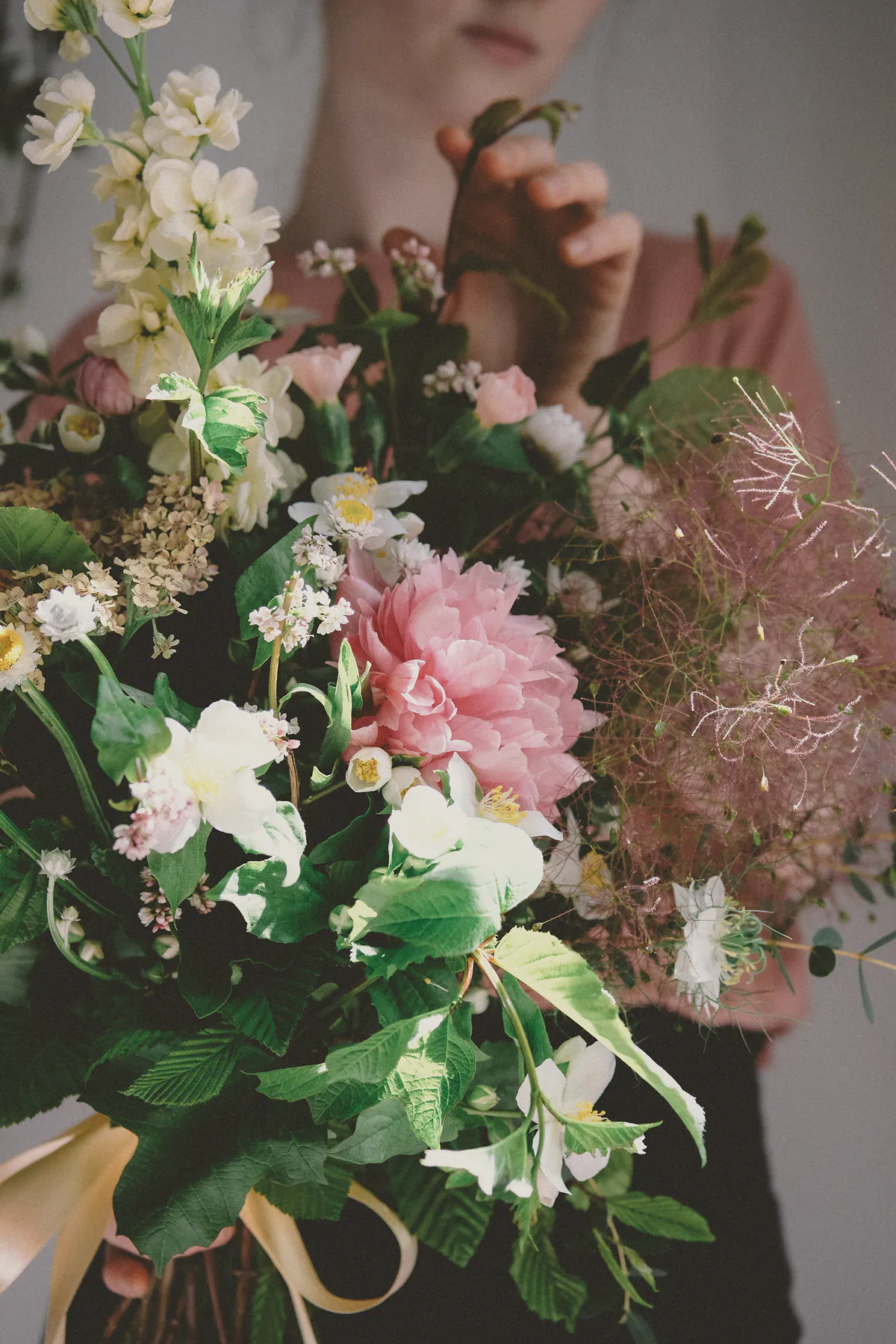 Hands holding a loose posy of pink dahlia, white cosmos and feathery smoke bush