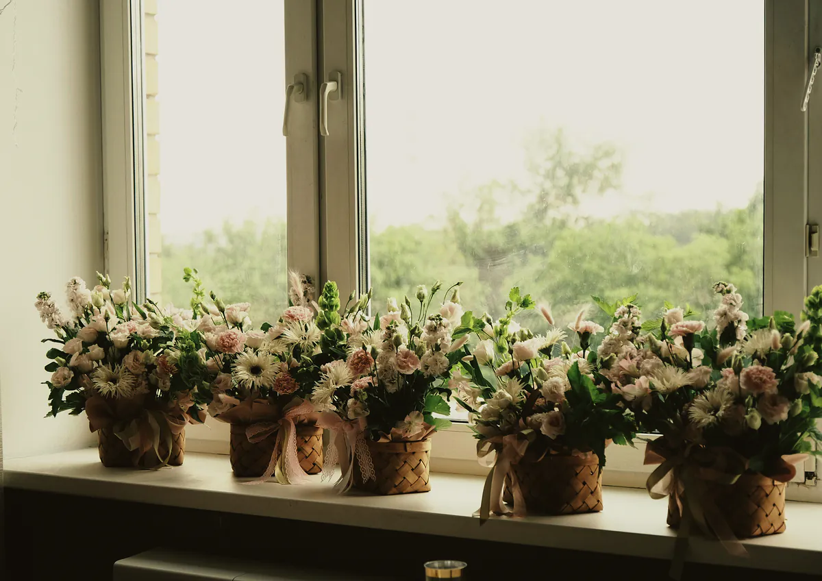 A row of small blush posies in woven baskets along a bright windowsill