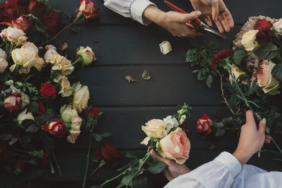 Hands trimming roses and greenery across a dark timber workshop table